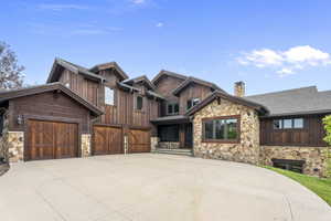 Craftsman inspired home featuring stone and cedar siding, heated concrete driveway, a chimney, and 3 car garage
