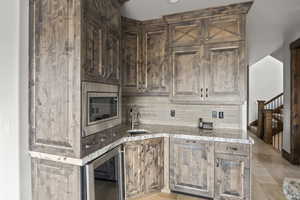 Kitchen with wine cooler, stainless steel microwave, backsplash, and light stone countertops