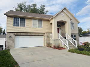 Raised ranch featuring brick siding, concrete driveway, and a garage