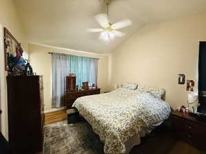 Bedroom with dark wood-style floors, ceiling fan, and lofted ceiling