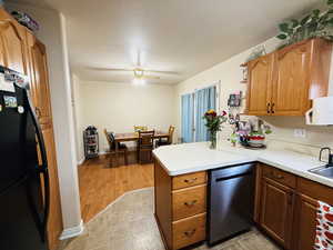 Kitchen with freestanding refrigerator, light countertops, brown cabinetry, stainless steel dishwasher, and a textured ceiling