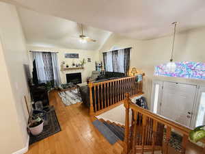 Living area with light wood finished floors, a tiled fireplace, vaulted ceiling, stairway, and ceiling fan