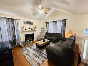 Living room with wood-type flooring, vaulted ceiling, a tile fireplace, and ceiling fan