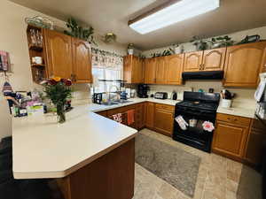 Kitchen with black range with gas stovetop, a peninsula, brown cabinetry, and light countertops