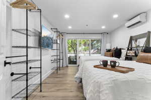 Bedroom featuring light wood finished floors, recessed lighting, a wall mounted AC, and access to outside
