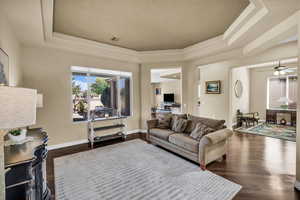 Living room with a raised ceiling, dark wood finished floors, a ceiling fan, and a textured ceiling