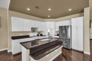 Kitchen featuring white appliances, dark wood finished floors, white cabinets, a kitchen island with sink, and recessed lighting