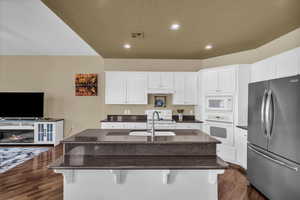 Kitchen featuring white appliances, a textured ceiling, white cabinets, dark stone countertops, and recessed lighting