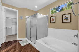 Full bath with a bath, a shower stall, dark wood-type flooring, a walk in closet, and recessed lighting