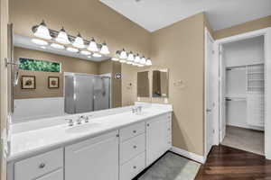 Full bath with dark wood-style flooring, double vanity, a shower stall, and a walk in closet