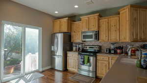 Kitchen with appliances with stainless steel finishes, dark wood-style floors, light brown cabinets, backsplash, and recessed lighting