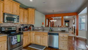 Kitchen featuring stainless steel appliances, light brown cabinetry, decorative backsplash, a chandelier, and hanging light fixtures