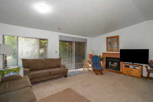 Living room with a tile fireplace, carpet flooring, a textured ceiling, and vaulted ceiling