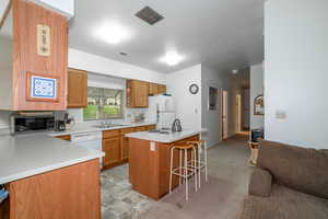 Kitchen with a center island, brown cabinets, light countertops, a breakfast bar area, and white appliances