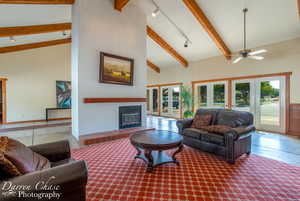 Living area featuring high vaulted ceiling, beamed ceiling, a glass covered fireplace, and ceiling fan