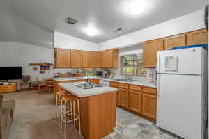 Kitchen with white appliances, a kitchen bar, open floor plan, light countertops, and vaulted ceiling