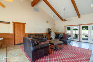 Living area featuring a ceiling fan, high vaulted ceiling, beam ceiling, and wainscoting