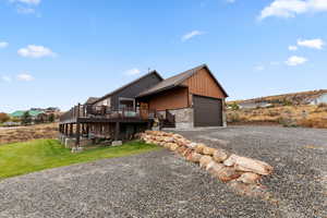 View of side of home featuring a wooden deck, stone siding, gravel driveway, stairs, and a yard