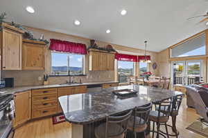 Kitchen with dark stone countertops, a center island, a breakfast bar, light wood-type flooring, and lofted ceiling