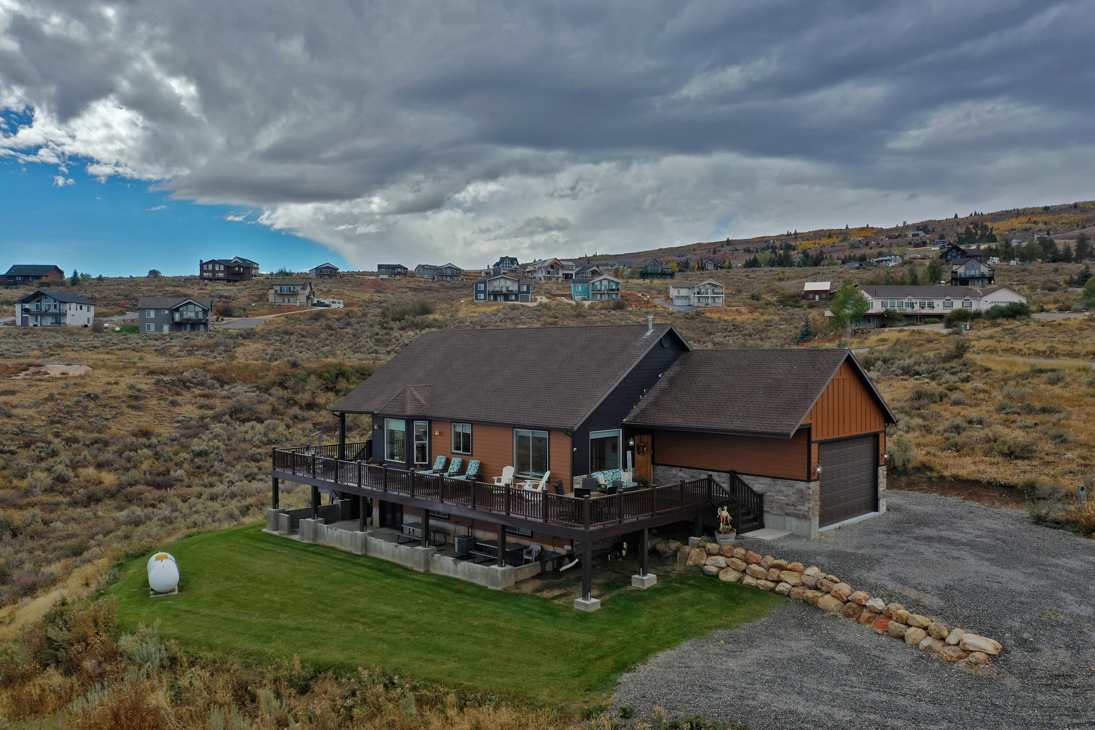 View of front of home featuring stone siding, a wooden deck, driveway, and a front lawn