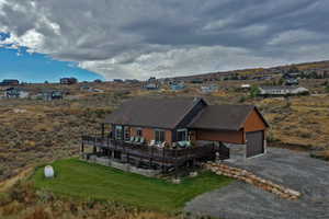View of front of home featuring stone siding, a wooden deck, driveway, and a front lawn