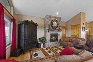 Living area with wood-type flooring, a stone fireplace, and high vaulted ceiling