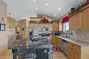 Kitchen with dark stone counters, light wood-style flooring, stainless steel appliances, lofted ceiling, and hanging light fixtures