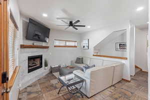 Living room with stone tile flooring, a tile fireplace, a ceiling fan, and recessed lighting