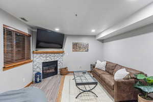 Living room with a stone fireplace, wood finished floors, and recessed lighting
