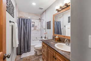Full bathroom with a textured ceiling, shower / tub combo, vanity, and dark stone finish floors