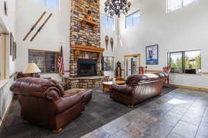 Living area with plenty of natural light, stone tile flooring, a towering ceiling, a fireplace, and a chandelier
