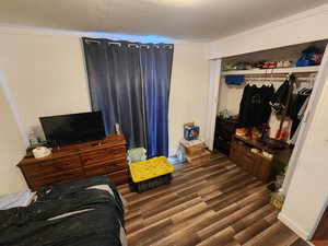 Bedroom with dark wood finished floors, ornamental molding, and a closet