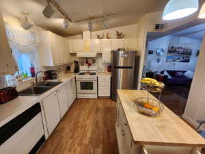 Kitchen featuring rail lighting, white cabinetry, white appliances, dark wood-type flooring, and vaulted ceiling