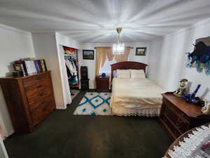 Carpeted bedroom with a closet, crown molding, a textured ceiling, and a chandelier