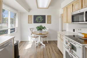 Kitchen with double oven range, light countertops, stainless steel microwave, light wood-style flooring, and light brown cabinets