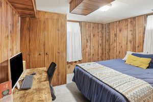 Carpeted bedroom with wooden walls and an office area