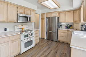 Kitchen featuring light brown cabinetry, appliances with stainless steel finishes, light countertops, and dark wood finished floors