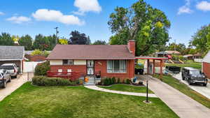 View of front of house featuring a front lawn, a chimney, brick siding, and concrete driveway