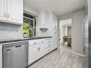 Kitchen featuring appliances with stainless steel finishes, white cabinets, light wood-style floors, and tasteful backsplash