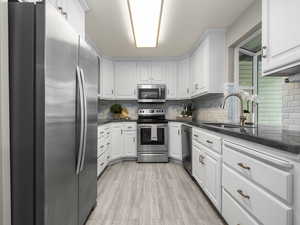 Kitchen with appliances with stainless steel finishes, dark stone counters, backsplash, and white cabinetry