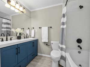Full bath with double vanity, light wood-style floors, crown molding, and shower / bathtub combination with curtain