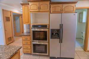 Kitchen with stainless steel appliances, dark stone counters, crown molding, light tile patterned floors, and light brown cabinets