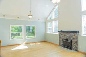Unfurnished living room with a stone fireplace, light wood finished floors, healthy amount of natural light, and high vaulted ceiling