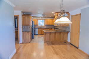 Kitchen featuring decorative light fixtures, a peninsula, tasteful backsplash, dark stone counters, and ornamental molding
