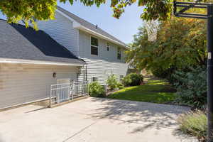 Rear view of property featuring a shingled roof, a patio, and a lawn