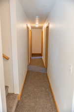 Corridor featuring dark carpet and stairs