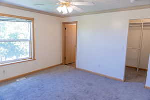 Unfurnished bedroom with crown molding, a walk in closet, light carpet, and a ceiling fan