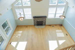 Unfurnished living room featuring high vaulted ceiling, a stone fireplace, and light wood finished floors
