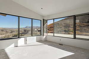 Unfurnished sunroom featuring lofted ceiling, a mountain view, and unfinished concrete floors