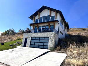 Modern home with stone siding, driveway, an attached garage, a balcony, and a front yard